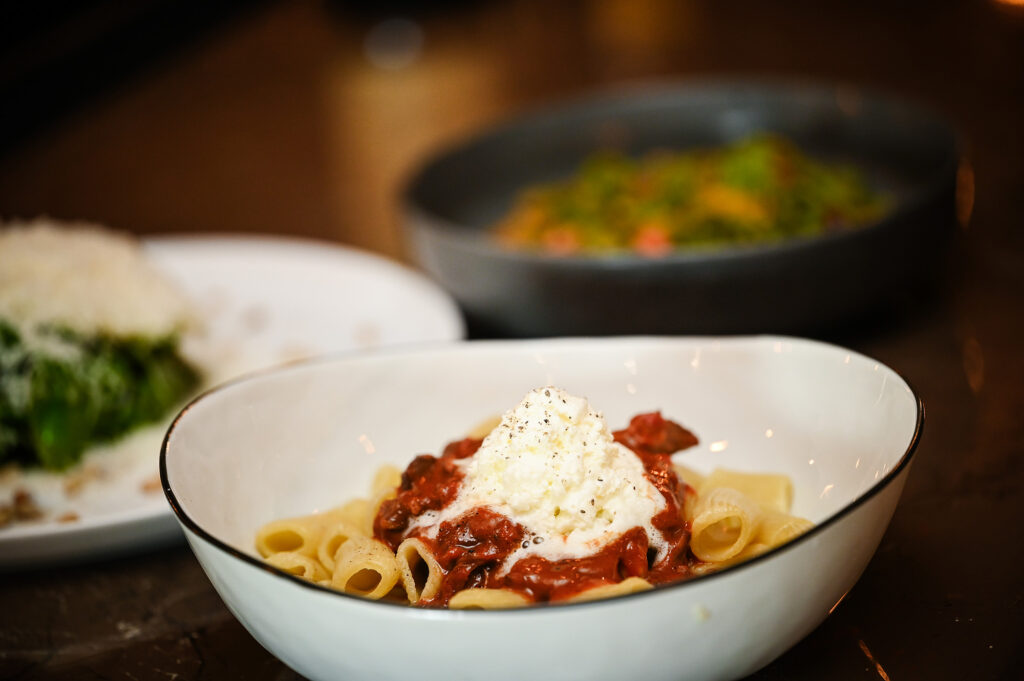 Photo of a bowl of pasta with sauce and cheese and two other plates of food in the background.