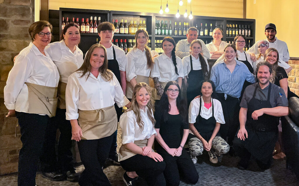 Photo of the entire staff of Lago Enoteca posing in front of shelves of wine.